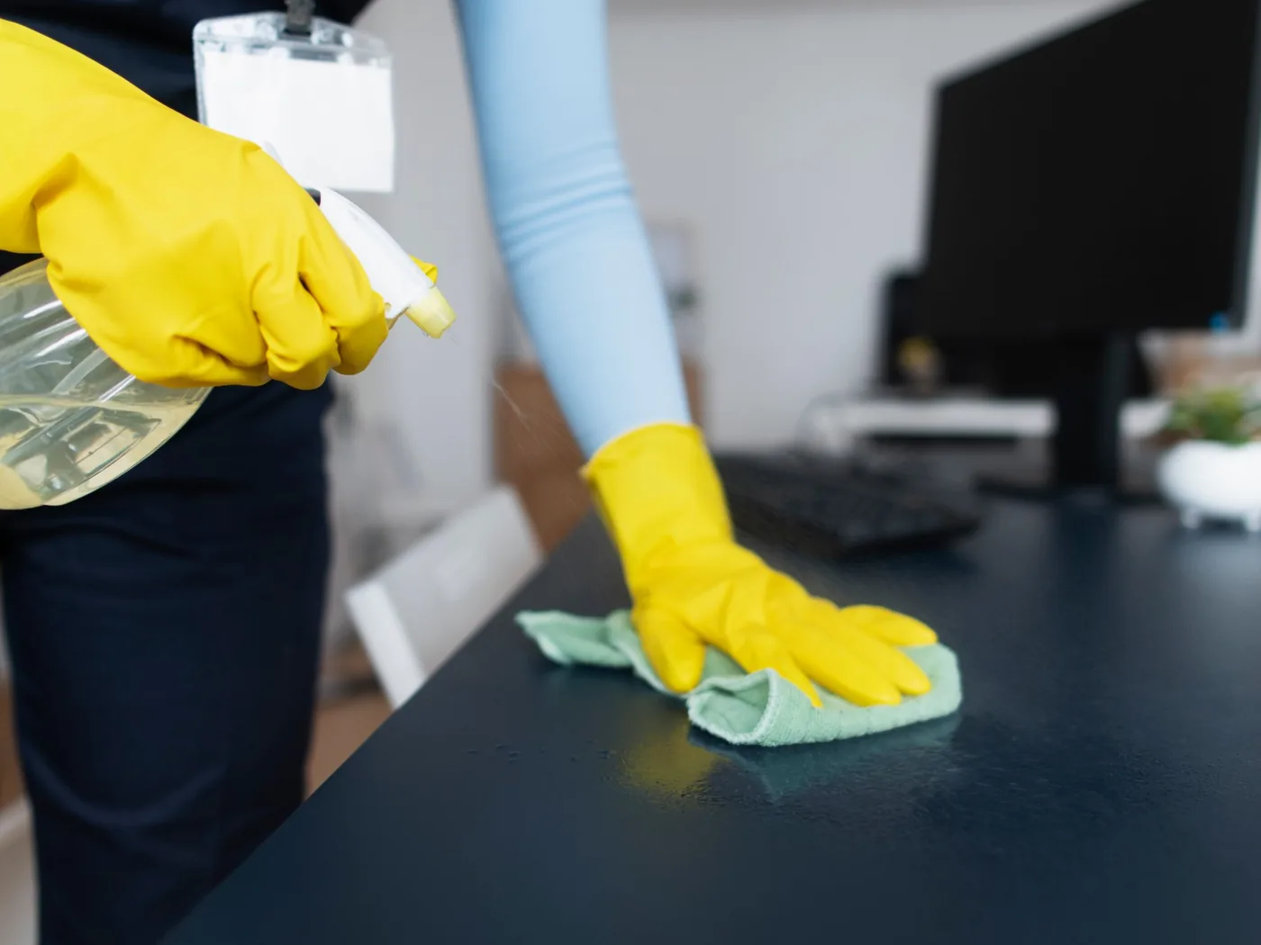A cleaner spraying and wiping down a desk in an office.