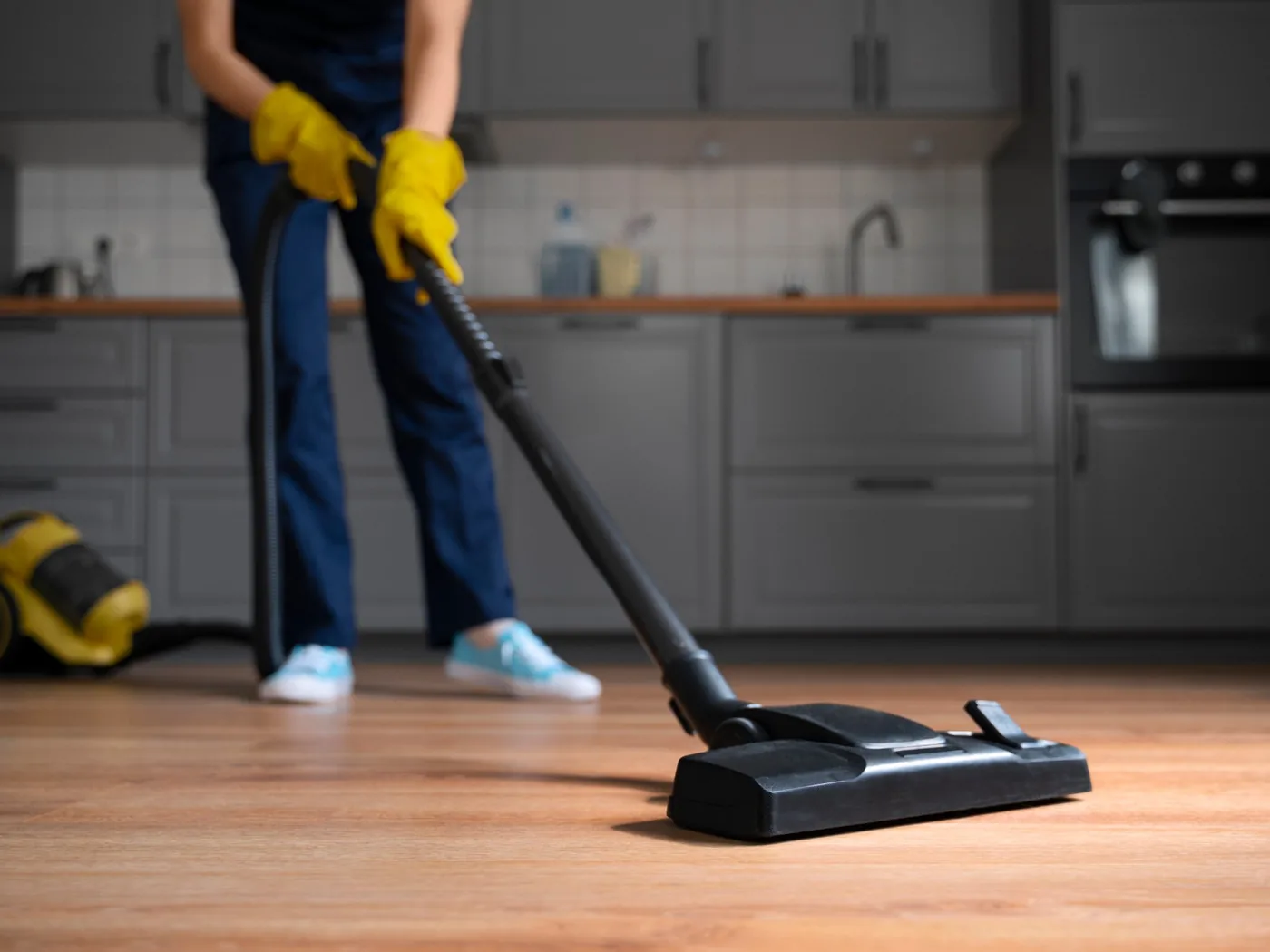 A cleaner vacuuming a wooden kitchen floor.