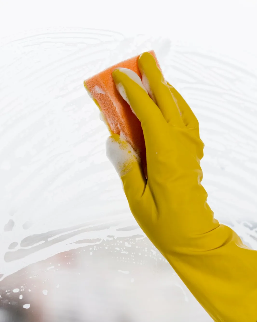 A gloved hand cleaning a pane of glass with a soapy sponge.