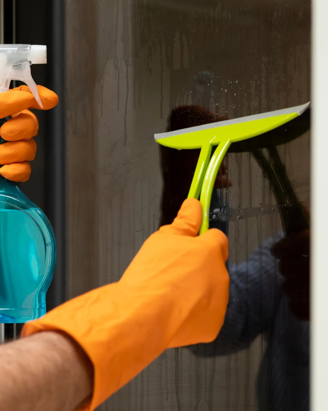 A cleaner using a squeegee and a spray bottle on a glass door.