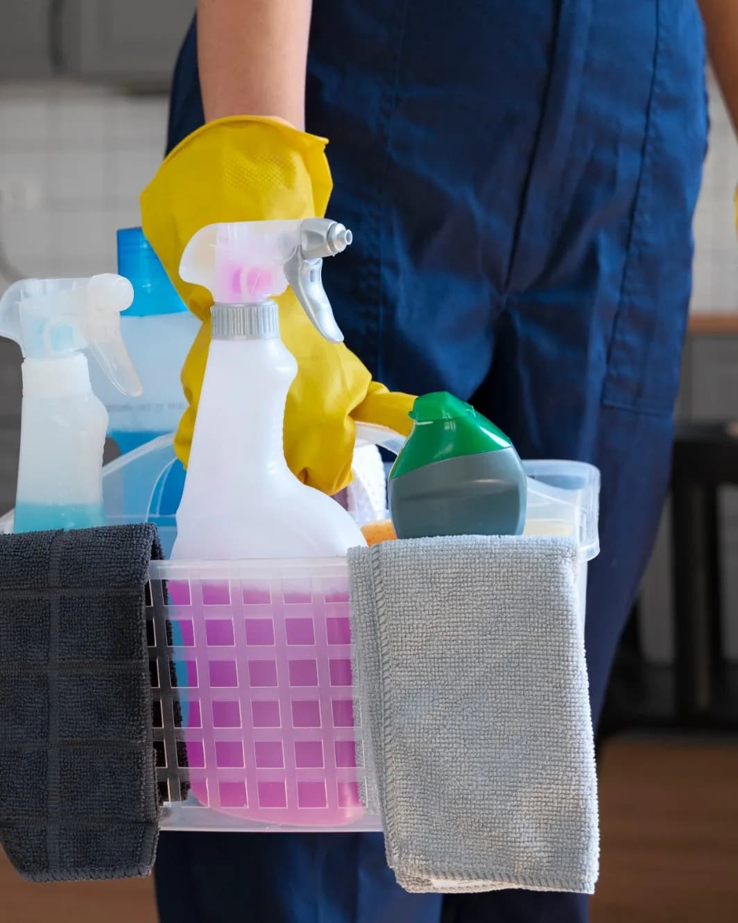 A cleaner carrying a basket of cleaning products and folded cloths.